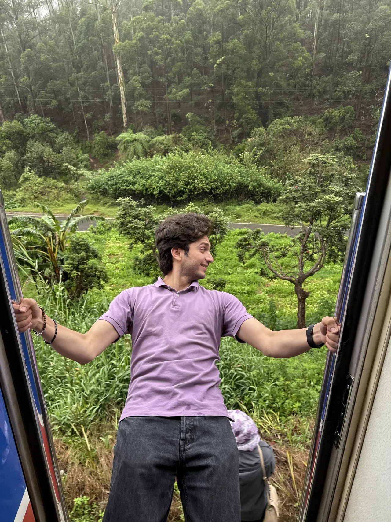 Monil leaning out of a moving train through green hills
